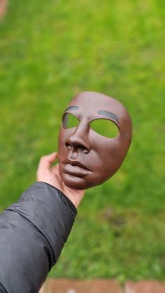 a person holding up a clay mask in front of their face with grass in the background