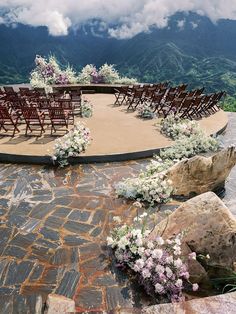 an outdoor ceremony set up with wooden chairs and flowers on the ground in front of mountains