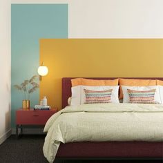 a bed with pillows and blankets on top of it next to a wall painted in different colors