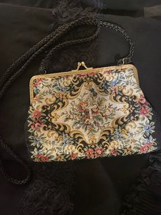 A vintage bag with an antique Victorian vibes look. This evening bag has a colorful needle point look (soft cloth fabric) in florals in front against a white background. It has a gold frame with a kiss clasp. Solid black in the back and it has a black cord like shoulder strap. *Rosary accent not included *Era: 1970's *Label: None *Fabric: Feels like cotton or a cotton blend *Condition: Gently used / No Flaws *Size: The bag measures 5 inches down and 8 inches across and it has a 19 inches strap Vintage Embroidered Clutch Evening Bag, Vintage Embroidered Shoulder Bag, Vintage Embroidered Pouch Bag, Vintage Multicolor Embroidered Shoulder Bag, Vintage Tapestry Pouch Bag, Vintage Tapestry Multicolor Shoulder Bag, Antique Tapestry Evening Bag, Vintage Tapestry Handmade Bags, Vintage Handmade Tapestry Bag