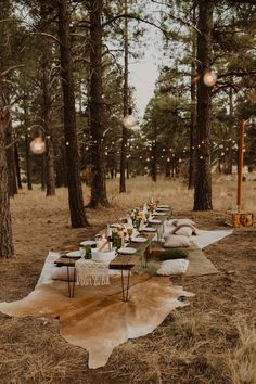 a long table is set up in the woods for an outdoor dinner with candles and lights