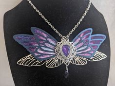 This gorgeous necklace features purple, black, and silver fairy wings with a opalescent purple gem in the middle. A drop crystal hangs from the center. Perfect for special occasions or to add a bit of magic to your everyday! Handmade Purple Fantasy Necklaces, Handmade Purple Fantasy Necklace, Purple Butterfly Charm Jewelry For Party, Magical Purple Pendant Necklace, Purple Fantasy Necklace For Gift, Fantasy Style Purple Necklace For Gift, Purple Gothic Necklace For Party, Gothic Purple Necklace For Party, Faerie Wedding