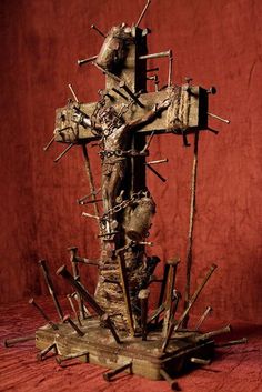 a wooden cross made out of sticks and nails on top of a red cloth covered surface