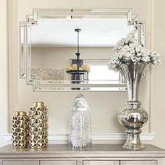 a silver dresser topped with vases and flowers next to a large mirror on the wall