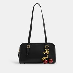 a black handbag with cherries hanging from the handle and two gold - tone handles