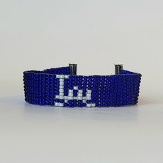 Show off your team spirit with this hand-beaded bracelet in the Dodgers' blue and white. This lightweight, loom-beaded bracelet is adjustable with a lobster claw clasp. It is made using Japanese glass seed beads and durable nylon thread. Please note that there may be some small differences in the digital representation of the item and the item itself. This can be caused by different people having varied monitor settings. Blue Beaded Bracelets For Team Spirit Gift, Blue Adjustable Bracelets For Team Spirit, Blue Team Spirit Beaded Bracelets As Gift, Blue Adjustable Beaded Bracelets For Team Spirit, Blue Beaded Bracelets With Letter Beads For Team Spirit, Crochet Dodgers Blanket, Blue Team Spirit Jewelry For Game Day, Dodgers Bracelet, Patriotic Blue Beaded Bracelets