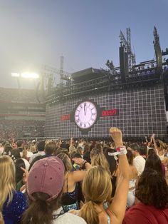 a crowd of people at a concert with a large clock on the wall