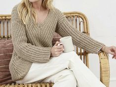 a woman sitting on a wicker chair holding a coffee cup