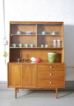 an old fashioned wooden cabinet with glass doors and drawers on it's sides, in front of a white wall