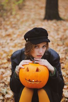 a woman sitting on the ground holding a pumpkin