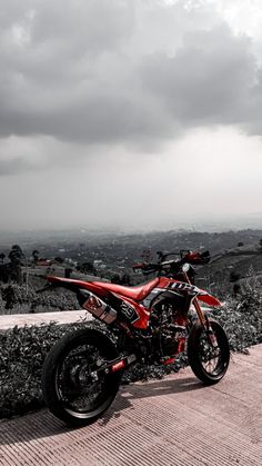 a red and black motorcycle parked on top of a brick road next to a lush green hillside