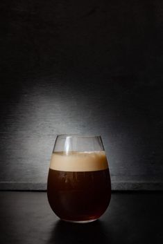 a glass filled with liquid sitting on top of a black table next to a wall