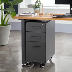 a computer desk with two drawers and a keyboard on the top, next to a potted plant