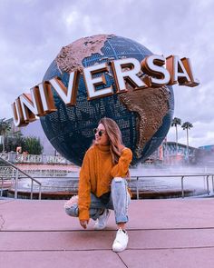 a woman sitting on the ground in front of a sign that says universal with a world globe behind her