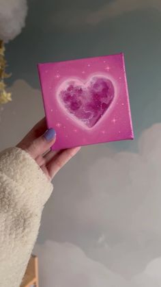 a person holding up a pink box with a heart on it's side and clouds in the background