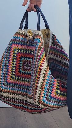 a person holding a multicolored crocheted bag in their hand while standing next to a wall