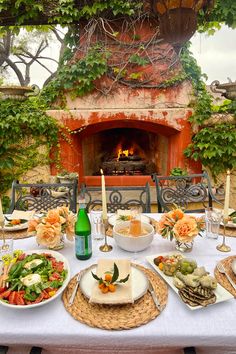 a table set with food and candles in front of an outdoor fireplace