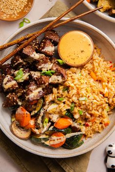 a bowl filled with rice, meat and vegetables next to chopsticks on a table