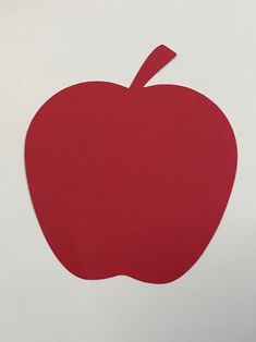 an apple cut out from red paper on a white surface