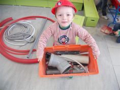 a young boy sitting on the floor with some tools in his hands and wearing a red hat