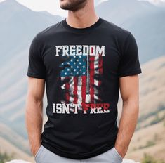 Honor the sacrifices of freedom with our "Freedom Isn't Free Shirt." This patriotic apparel showcases a powerful statement in bold typography, reminding everyone of the value of our hard-won liberties.  We use BELLA + CANVAS 3001, this shirt offers both style and comfort. Its soft, breathable fabric ensures a cozy fit, while its durable construction guarantees long-lasting wear. The design features the impactful phrase "Freedom Isn't Free," serving as a daily reminder of the sacrifices made for our rights. Available in different sizes and colors, this shirt is a perfect addition to your wardrobe. Wear it on patriotic holidays, to community events, or as a symbol of your unwavering support for liberty. It also makes a meaningful gift for friends and family who cherish the principles of inde Black T-shirt With American Flag For 4th Of July, Black Patriotic Shirt With Letter Print, Patriotic Black Top With Flag Print, Patriotic Black T-shirt For Veterans Day, Patriotic Black Crew Neck Shirt, Black Patriotic Crew Neck Shirt, Black Crew Neck Patriotic Shirt, Patriotic Black Shirt With Graphic Print, Black Patriotic Shirt With Graphic Print