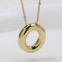 a gold necklace with a circular design on it's chain, hanging from a white background