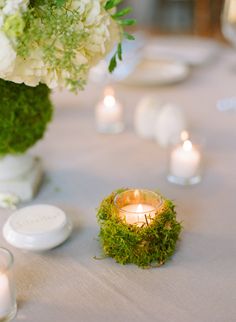 a table topped with a vase filled with white flowers and greenery next to candles