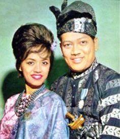 two people standing next to each other in front of a green wall and one person is wearing an elaborate headdress