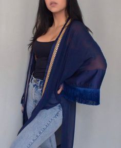 Dark blue oversized kimono with fringe details on the sleeves and an embroidered trim detail.  This kimono was made for those who live life on the go. The oversized silhouette makes it perfect for those long days exploring new cities or lounging at the beach. The fringe and embroidered trim add a touch of fun and personality, while the side slits make it easy to move around. Whether you're packing it for your next trip or wearing it around town, this kimono will make you feel like the wanderlust Spring Fringed Long Sleeve Kimono, Spring Fringe Long Sleeve Kimono, Bohemian Long Sleeve Kimono With Fringe, Spring Long Sleeve Fringed Kimono, Fall Beach Kimono With Tassels, Festival Long Sleeve Kimono With Fringe, Fringe Kimono For Beach In Fall, Long Sleeve Festival Kimono With Fringe, Long Sleeve Fringe Kimono For Festivals