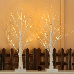 three white trees with lights in them on a mantle