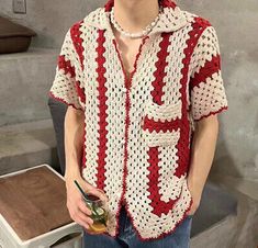 a man wearing a red and white crochet shirt holding a drink in his hand