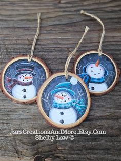 three snowman ornaments hanging from wood slices on a table with string and twine