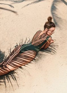 a woman laying on top of a sandy beach next to a palm frisbee