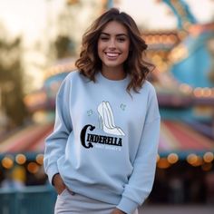 a woman wearing a blue sweatshirt with the word cinderella printed on it in front of a carnival ride