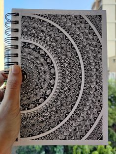 a hand holding up a spiral notebook with black and white designs on the front cover