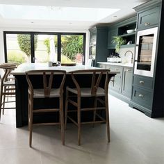 a kitchen with an island and bar stools next to it, in front of large windows