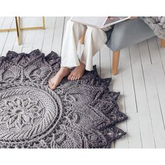 a woman is sitting on the floor with her feet propped up in front of a crocheted rug