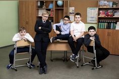 four boys in suits and ties are sitting at desks with their arms crossed, looking to the side