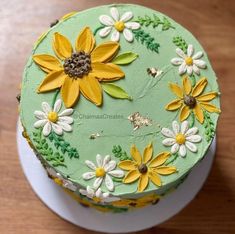 a green cake with yellow and white flowers on it sitting on a wooden table top