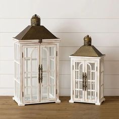 two white lanterns sitting next to each other on a wooden table in front of a wall