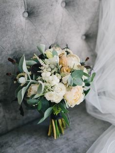 a bridal bouquet sitting on top of a gray couch next to a white tulle