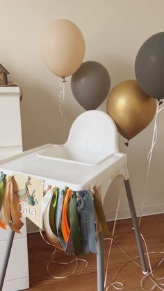 a baby's highchair with balloons in the air and clothes hanging from it