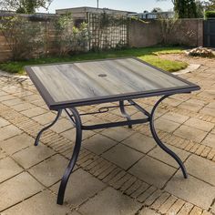 an outdoor table sitting on top of a brick patio next to a fenced in yard