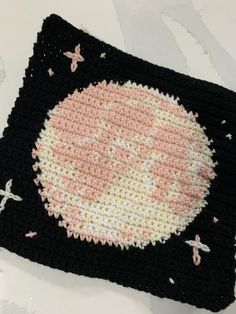 a crocheted black and white square with a pink face on the front, surrounded by small stars