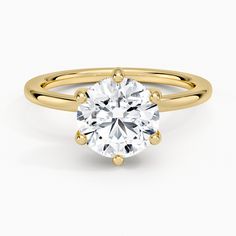 a yellow gold engagement ring with a round cut diamond in the center, on a white background