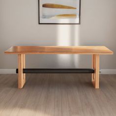 a wooden table sitting on top of a hard wood floor next to a painting hanging above it