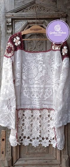 a white crocheted top with flowers on the collar and sleeves, hanging from a wooden hanger