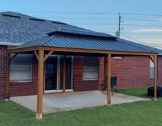 a patio covered with a metal roof in front of a brick building and green grass