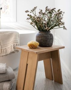 a vase with flowers sitting on top of a wooden stool next to a bath tub