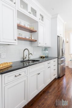 a kitchen with white cabinets and black counter tops, wood flooring and stainless steel appliances